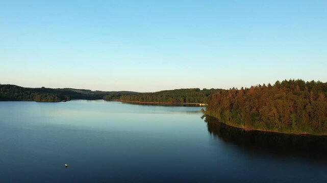 Scenic aerial shot of Lac des Settons with calm water and lush forest shoreline under a clear evening sky in Burgundy, France.