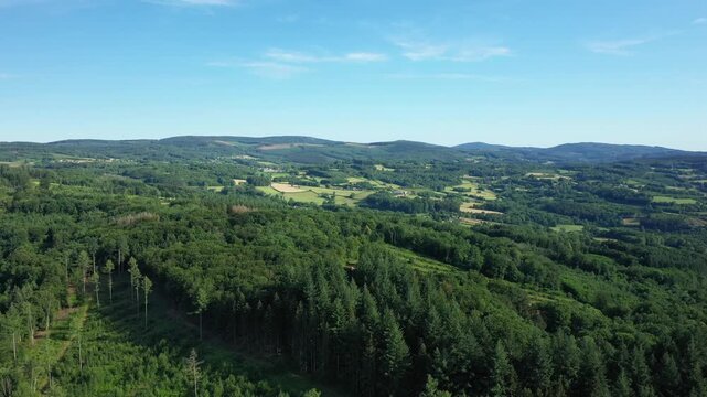 Scenic aerial view of lush green forests and rolling hills in the Morvan countryside under a clear blue sky.