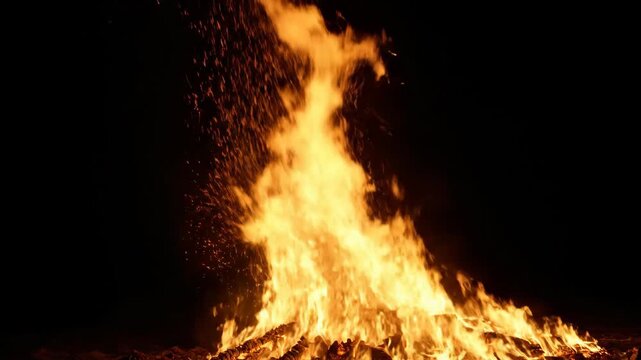 Massive bonfire ablaze at night with flames and sparks on black background. Fire, night, sparks, flames, wood, burning.