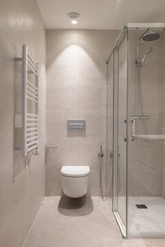 Modern bathroom with a glass shower, white toilet, and towel radiator. Neutral color scheme with tiled walls and floor. Clean and minimalist design.