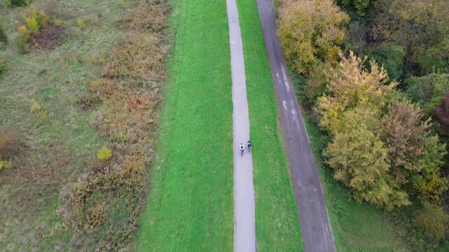 Aerial view of two cyclists riding along a scenic path surrounded by vibrant autumn foliage, showcasing the beauty of nature, camera follows with a smooth dolly motion