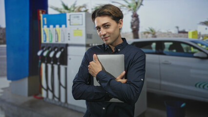 Man holds laptop hugging it to his chest at a street gas station forecourt with fuel pumps and a parked car  mobile work contentment. © Krakenimages.com