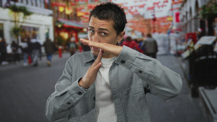 Fototapeta premium Young man making time-out gesture on bustling urban street with festive decorations and diverse crowd walking by