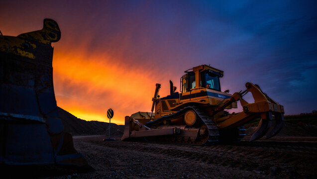 Heavy bulldozer working on a construction site at dramatic sunset with vibrant sky.