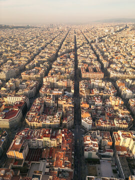 Aerial view of the grid-like expanse of Eixample district stretches towards the horizon, the sun kissing the rooftops with a warm glow, Barcelona, Catalonia, Spain.