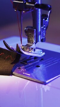 A seamstress removes a piece of stitched fabric from the foot of a sewing machine - a red thread