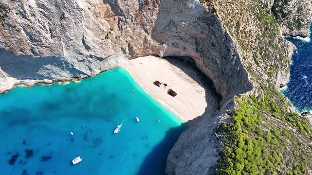 Aerial drone view of famous Navagio Shipwreck Beach with turquoise sea water and boats in Zakynthos island, Greece on a bright sunny da