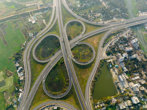 Aerial view of the cloverleaf interchange's concrete curves cut through the green landscape, creating a complex web of connectivity, Bhanga, Dhaka Division, Bangladesh.