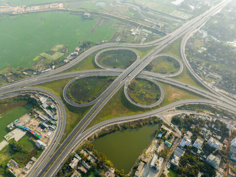 Aerial view of a cloverleaf interchange with sleek asphalt curves amidst the greenery, where roads converge like ribbons, Bhanga, Dhaka Division, Bangladesh.