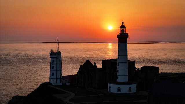 Aerial view of Saint-Mathieu Lighthouse and Semaphore standing by the abbey ruins as dark sentinels against the fiery sunset over the sea, Plougonvelin, Brittany, France.