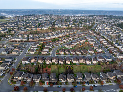 Aerial view of neat rows of houses with dark roofs and light walls, interspersed with green spaces and winding roads, Lake Tapps, Washington, United States.
