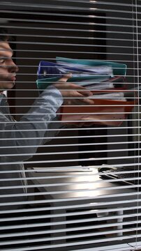 Vertical video businessman carrying a stack of confidential documents and folders, leaving a dark office, suggesting corporate espionage, information theft, or an unauthorized data breach