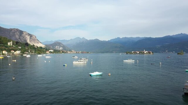 Several boats float on the calm waters of Lake Maggiore with Isola dei Pescatori and scenic mountains in the background. The tranquil setting highlights the beauty of this Italian lakeside destination