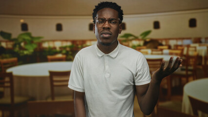 Obraz premium African american man wearing white polo shirt raising right hand gesture inside restaurant building; confusion.