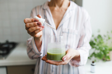 Hands of unrecognizable mature female adding liquid collagen dietary supplement with pipette into...