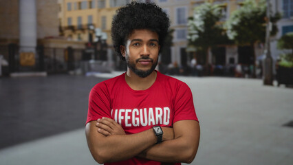 Man in lifeguard shirt stands confidently on a city street surrounded by urban buildings and trees, exuding confidence in a vibrant and lively outdoor setting. © Krakenimages.com