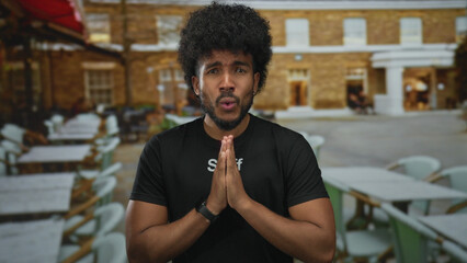 African american man in staff uniform stands praying on a restaurant terrace in an outdoor setting. © Krakenimages.com