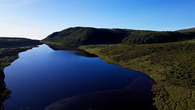 Aerial view of the calm, dark waters of Lake Ellis reflect the clear sky, nestled among the rolling green hills of Mt. Kenya, Lake Ellis, Meru County, Kenya.