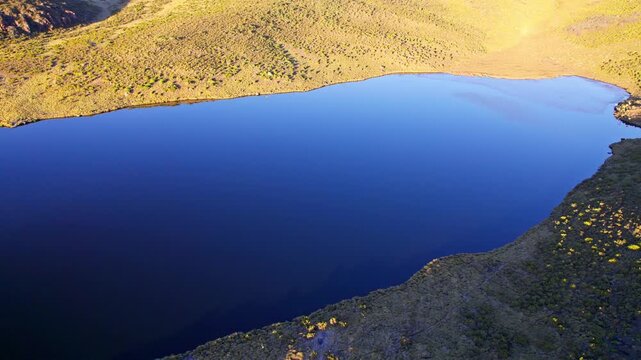 Aerial view of Lake Ellis, Mt Kenya, with dark blue water reflecting the sky and surrounding golden-green terrain, Lake Ellis, Meru County, Kenya.