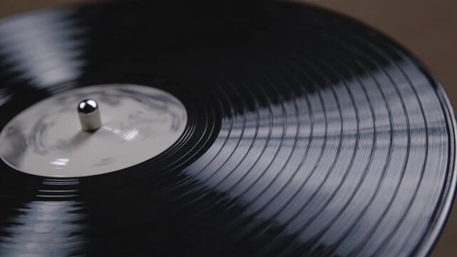 Close-up view of spinning vinyl record on turntable showcasing grooves and label, with reflections and textures visible in a softly lit indoor setting