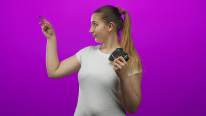 Woman holding a gamepad points finger to the side while smiling, wearing a white t shirt in studio  playful confidence. © Krakenimages.com
