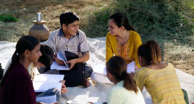 Indian villager girl boy sitting on mat do study read book outdoor rural area ground place. Happy group child hold notes talk gossip enjoy desi life new day outside open class field