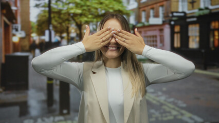 Fototapeta premium Woman smiling playfully covering her eyes in a vibrant city street setting, exuding joy and a carefree attitude, captured outdoors in an urban environment for a fun lifestyle concept.