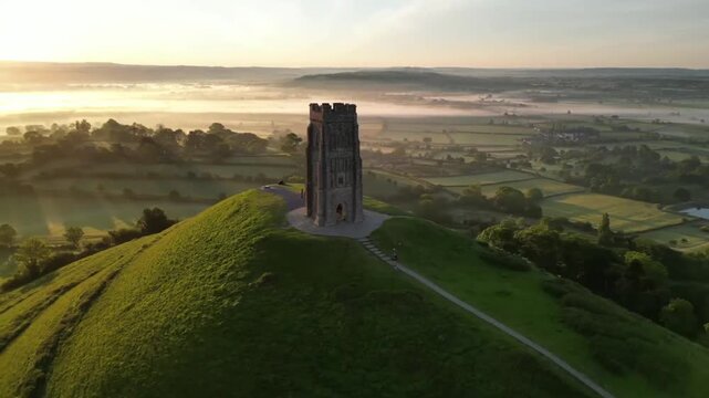 Aerial View of Glastonbury Tor at Sunrise with Sun Rising Behind St Michaels Tower and Misty Somerset Levels