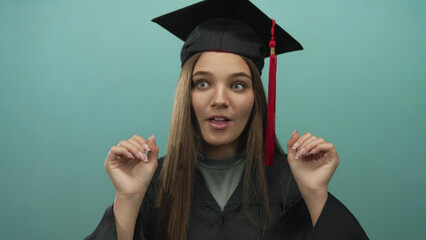Fototapeta premium Young graduate woman rubbing her eyes with graduation cap and gown in studio with teal backdrop; tiredness success.