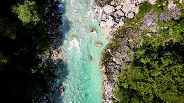 Aerial view of the turquoise Soca River surrounded by lush green forests and rocky riverbanks, creating a vivid contrast of colors, Kobarid, Tolmin, Slovenia.