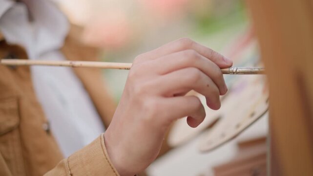 closeup painter applying vibrant green strokes on canvas, palette in hand and brush tip loaded with pigment, jacketed artist working outdoors in park setting, energetic color study with lively motion