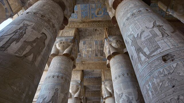 Dendera temple or Temple of Hathor. Painted columns with goddess faces and hieroglyphic ceiling of the hypostyle hall, ancient architecture with detailed carvings and blue painted zodiac. Egypt.