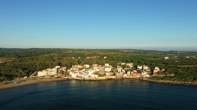 Aerial view of the picturesque seaside village of Arkoudi, Greece, surrounded by lush greenery and calm waters under a clear blue sky.