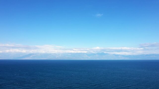 Wide view of the deep blue sea with distant mountains under a clear sky, captured near Koroni, Greece. Tranquil seascape ideal for travel and nature concepts.