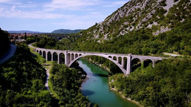 Aerial view of the Solkan bridge over the turquoise Soca river, connecting lush green riverbanks and the rocky mountain, Solkan, Nova Gorica, Slovenia.