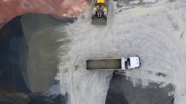 Aerial view of a bright yellow bulldozer filling a truck with soil amidst the textured landscape of a construction site, Plouasne, Brittany, France.