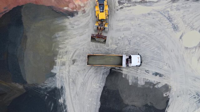 Aerial view of heavy machinery and a truck moving through a mine site with piles of colorful materials, Plouasne, Brittany, France.