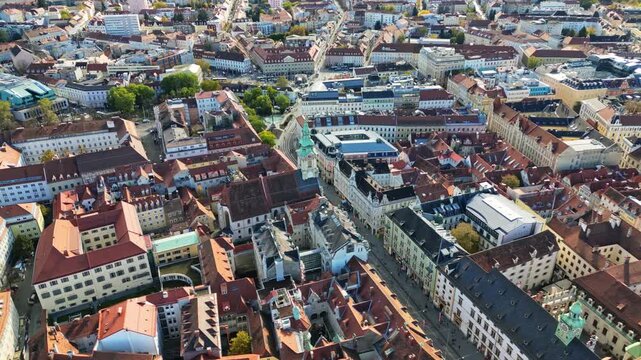 Aerial view of buildings with red roofs and a church with green tower, creating a vibrant tapestry of urban life, Graz, Styria, Austria.