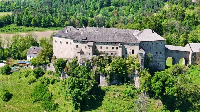 Aerial view of a castle perched atop a hill, its stone walls contrasting with the lush green trees, River Drau, Ferlach, Carinthia, Austria.