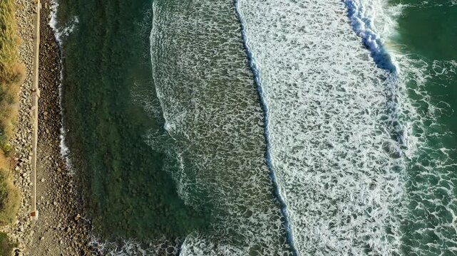 Drone shot of waves crashing on a rocky shoreline in Acciaroli, Italy. Clear turquoise water and rugged coast create a natural scenic landscape.