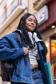 Young smiling black student walking in the city with books and backpack