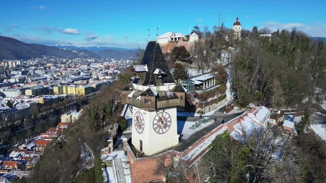 Aerial view of the Grazer Uhrturm clock tower standing tall, overlooking the snow dusted city with the Schlossberg hill, Graz, Styria, Austria.