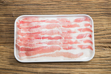 Thin raw pork belly slices are lined on a white tray over rustic wood. The pink and white marbling suggests freshness, ready for hot pot, stir fry or grilling.
