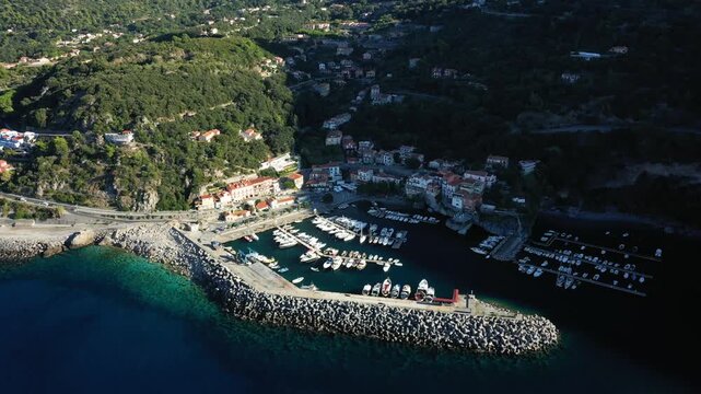 Scenic aerial shot of the marina and coastal village at Maratea Port in southern Italy, surrounded by lush green hills and clear blue sea.