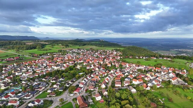 Aerial view of houses with red roofs amid lush green fields, creating a picturesque scene under a cloudy sky, Erkenbrechtsweiler, Baden-Wurttemberg, Germany.