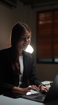 Focused businesswoman working late at night in a dimly lit office, typing on her laptop computer to meet a deadline. Concentrated employee is dedicated to her work after hours in the company office