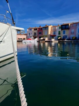 Grimaud,France - Febrary 18,2026:White yaht moored on calm water at the Grimaud port,colourful houses and small boats near