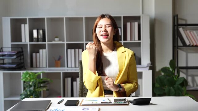 Happy asian businesswoman working on a tablet and using a calculator at her office desk, expressing excitement and joy after achieving a successful financial result for her company
