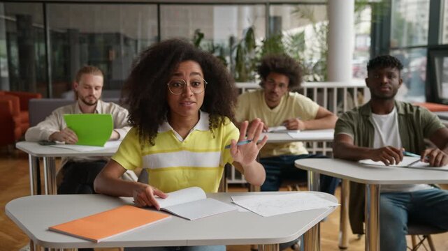 African American student girl nerd clever woman raising arm answering talking to teacher in class auditorium four multiethnic students at tables studying learning at lesson education study university