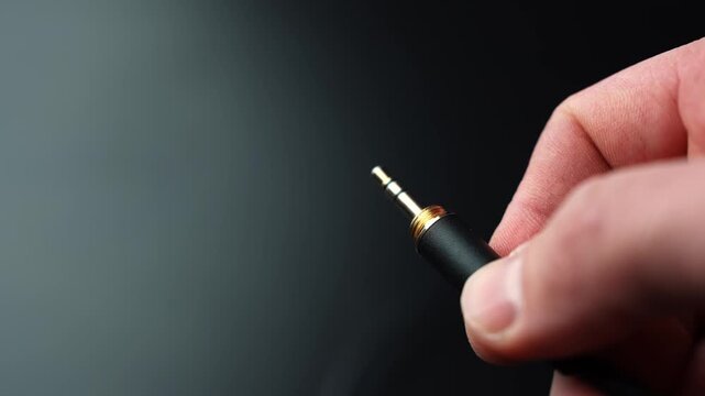 Hand holds a 3.5mm TRS audio plug on a dark backdrop with generous copy space, perfect for analog sound, studio wiring, and audio connection concepts.